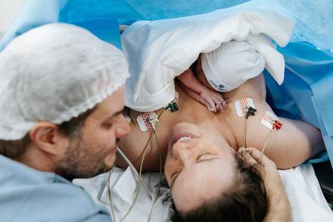 Casal emocionado com o bebê no colo materno logo após o nascimento.'