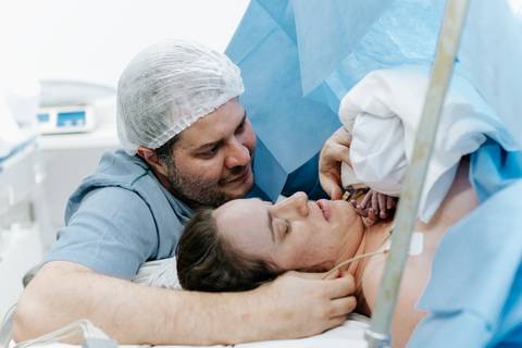 Pai acariciando o rosto da mãe enquanto o bebê repousa sobre ela.'