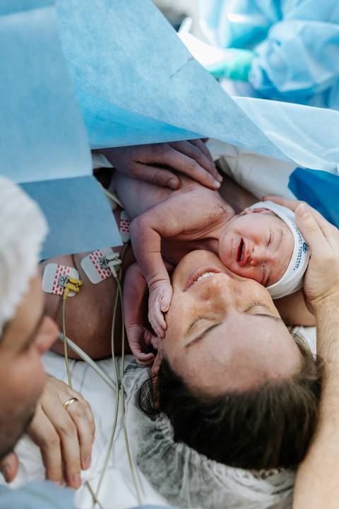 Mãe abraçando o bebê com ternura no pós-parto imediato.'