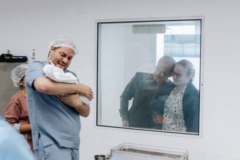 Pai apresentando o bebê para a família através do vidro do visor.'