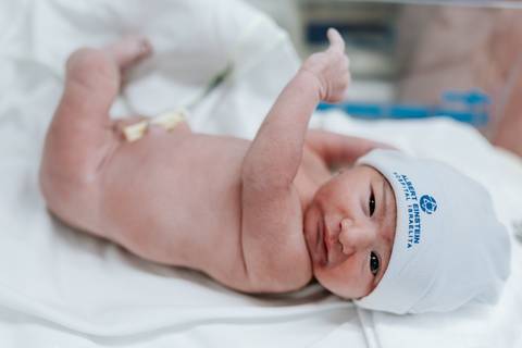 Recém-nascido deitado no berço hospitalar após os primeiros cuidados.'