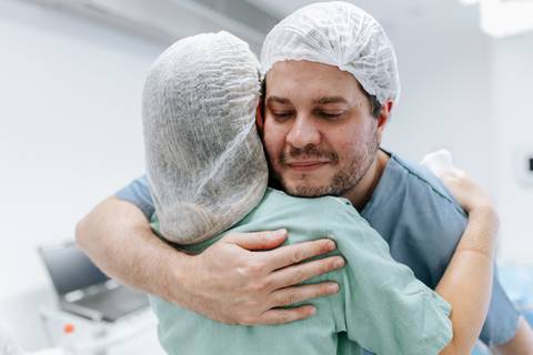 Pai abraçando emocionadamente uma profissional da equipe médica.'