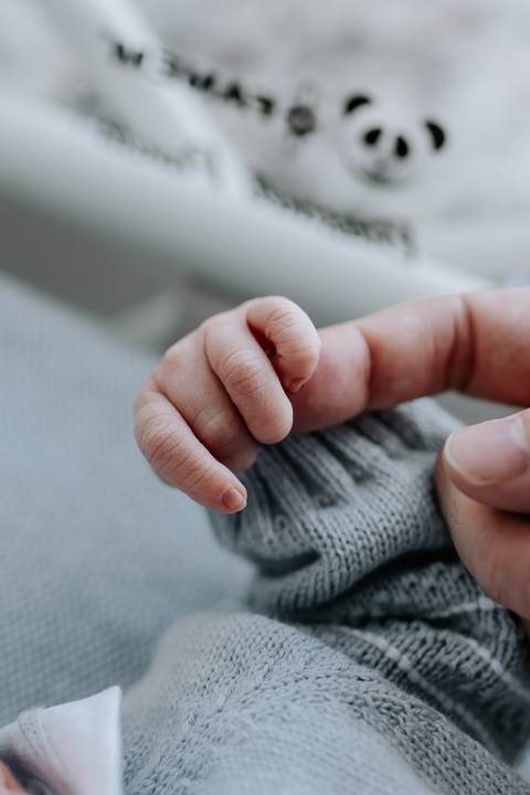 Detalhe da mãozinha do bebê segurando o dedo do pai.'