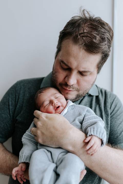 Close do pai segurando o bebê Guilherme no colo com carinho.'