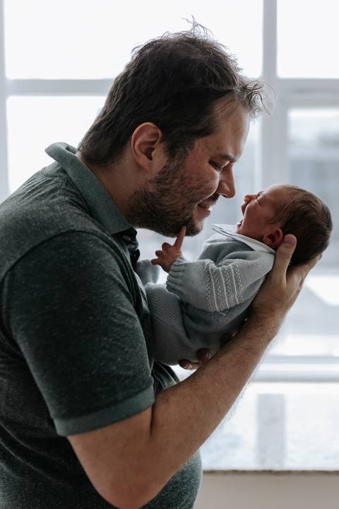 Pai aproximando o rosto do filho enquanto o segura no colo.'