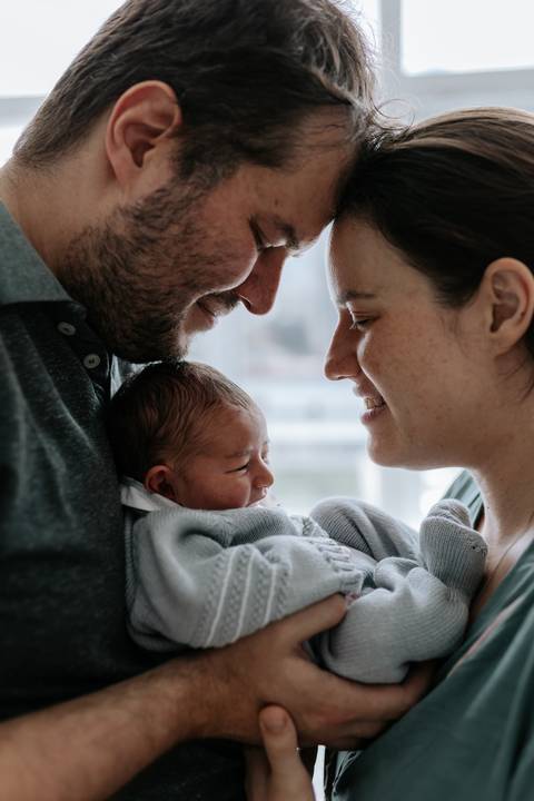 Casal trocando olhares carinhosos com o bebê entre eles.'