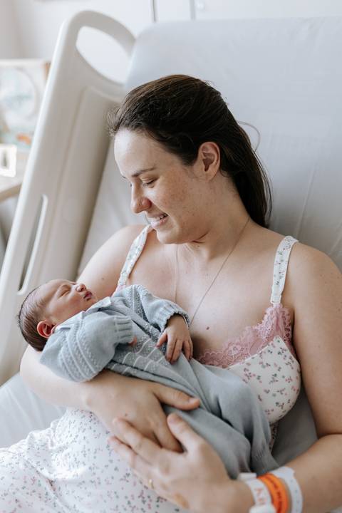 Mãe observando o filho dormir tranquilamente em seu colo.'