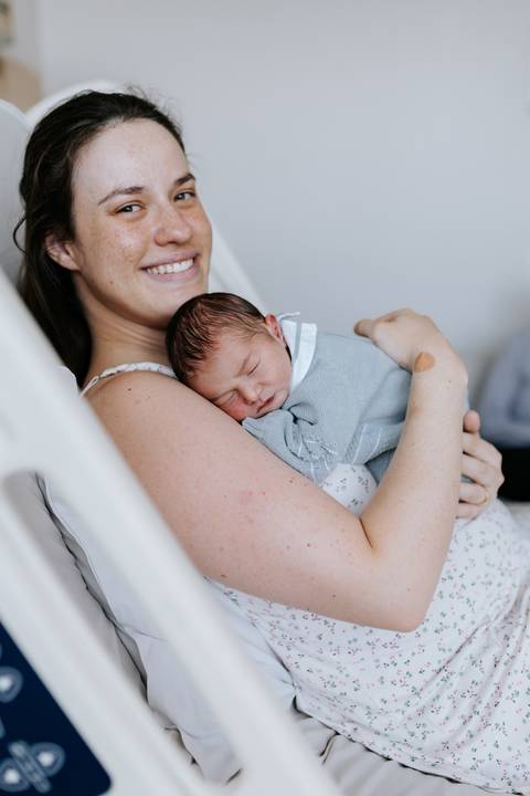 Mãe sorridente abraçando o bebê Guilherme contra o peito.'