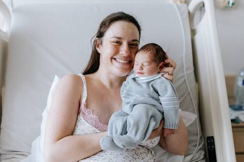 Mãe radiante segurando o filho no colo na cama da maternidade.'