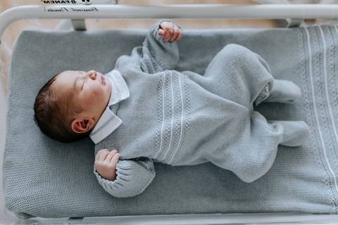 Bebê deitado de corpo inteiro com sua saída de maternidade azul.'