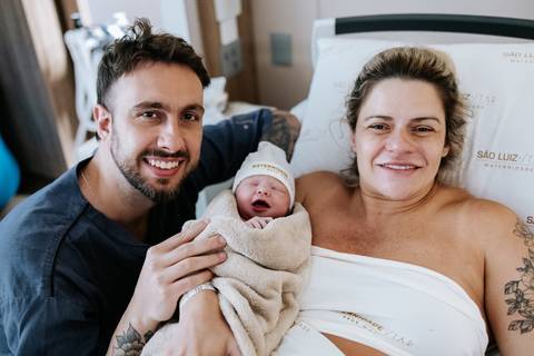 Foto do casal sorridente segurando a filha no colo.'