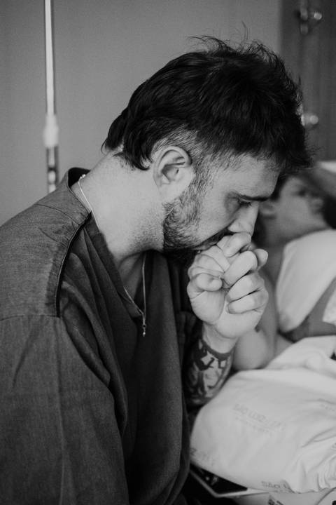 Foto em preto e branco do parceiro beijando a mão da gestante.'