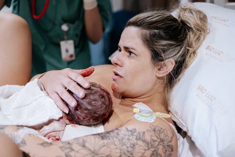 Foto da mãe emocionada ao receber a bebê no colo.'