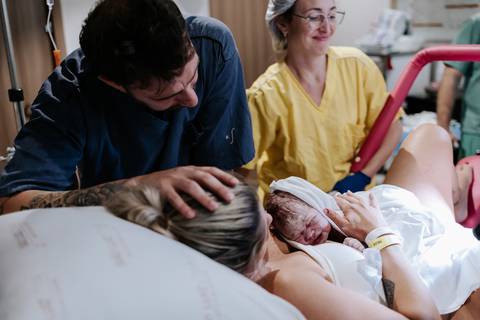 Foto do casal observando a recém-nascida logo após o parto.'