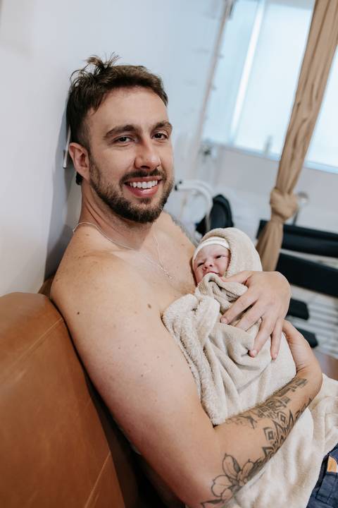 Foto do pai sorrindo durante o contato pele a pele com a bebê.'