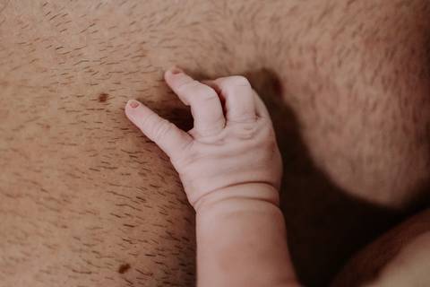 Foto da mão da bebê sobre o peito do pai no contato pele a pele.'