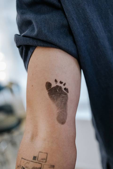 Foto do carimbo do pezinho da bebê no braço do pai. '