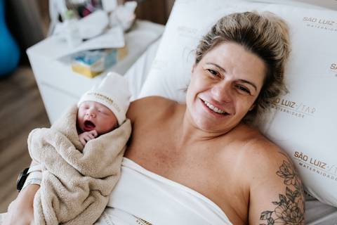 Foto da mãe radiante com a recém-nascida no colo. '