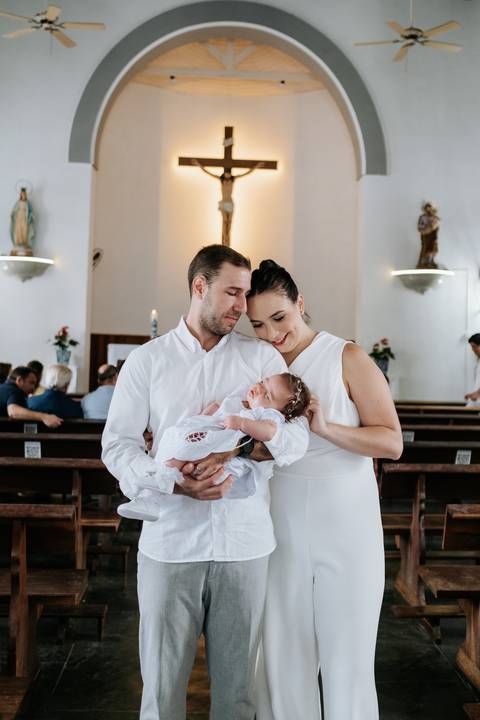Foto dos pais abraçados com a bebê no centro da igreja.'