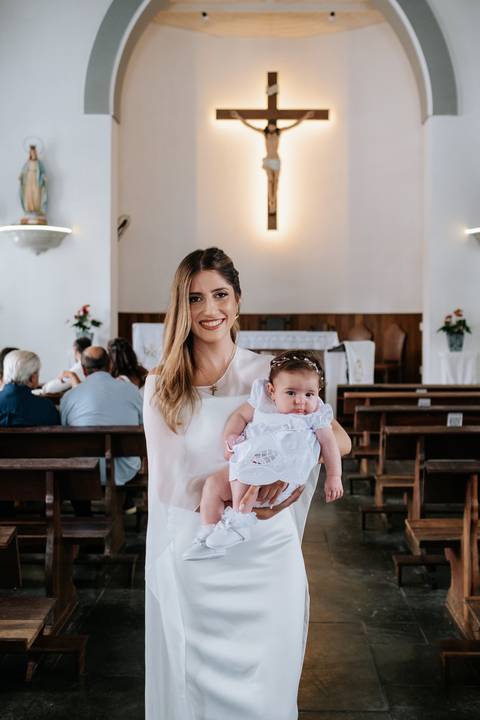 Foto da madrinha com a bebê no colo nos bancos da igreja.'