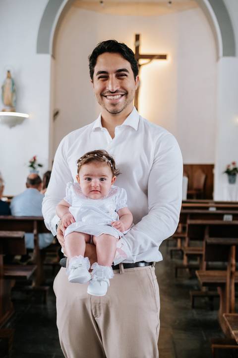 Foto do padrinho segurando Olívia de frente para a câmera.'
