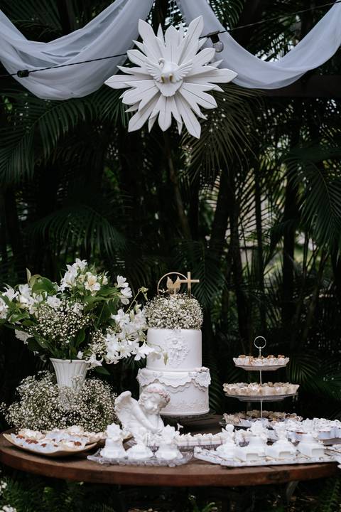 Foto da mesa de doces decorada com flores brancas e bolo.'