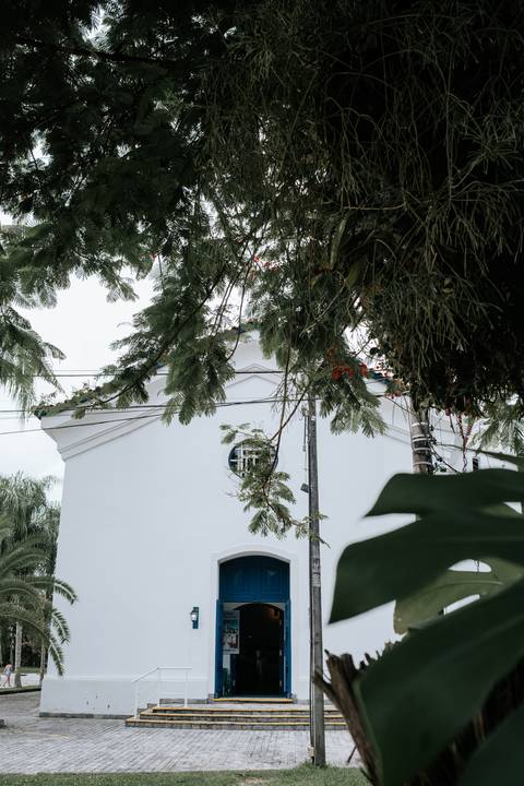 Foto da fachada da igreja entre as folhagens das árvores.'