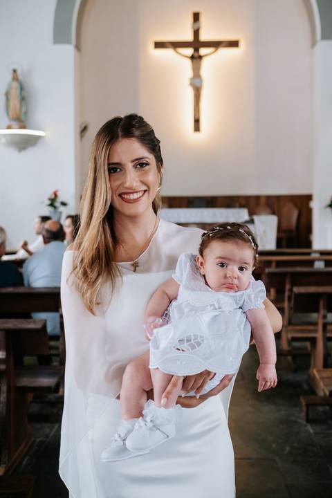Foto da madrinha segurando a bebê durante a cerimônia.'