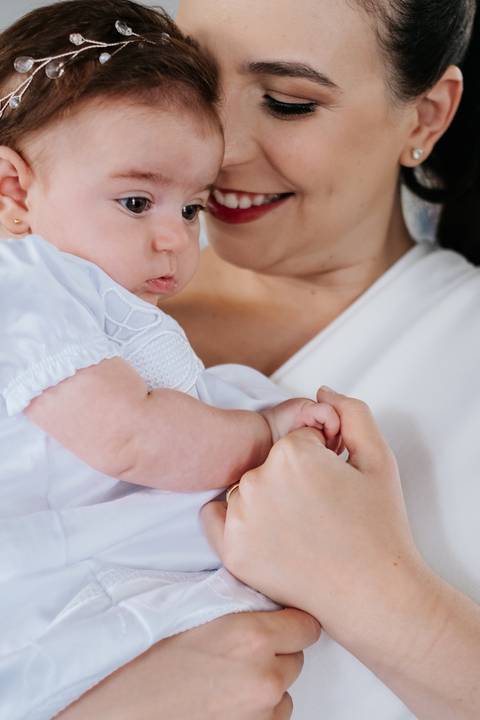 Foto em detalhe da mão da mãe segurando a mãozinha da bebê.'