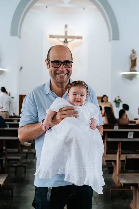 Foto do avô segurando Olívia sorridente nos bancos da igreja.'