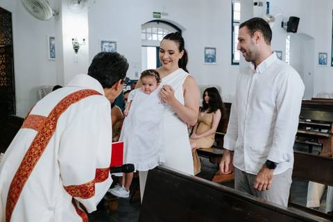 Foto do padre interagindo com a família durante a cerimônia.'