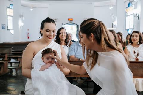 Foto da madrinha fazendo o sinal da cruz na testa da bebê.'