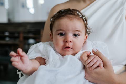 Foto de close da bebê Olívia com seu vestido de batismo.'