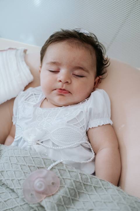 Foto de close da bebê Olívia dormindo calmamente com seu vestido bordado.'