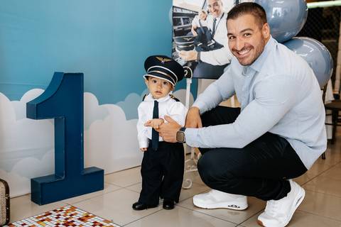 Foto do pai agachado ao lado do aniversariante vestido de piloto.'