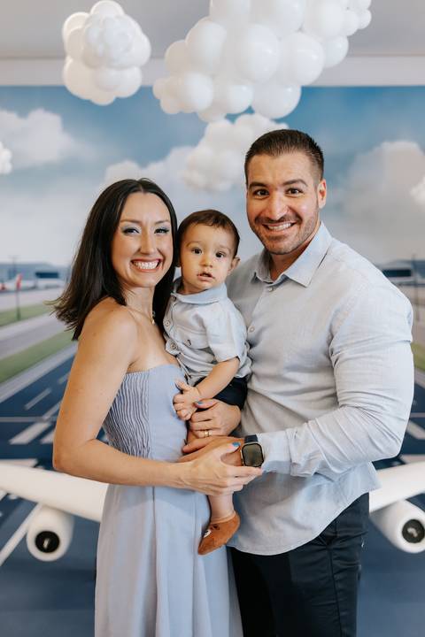 Foto dos pais sorridentes com o aniversariante no centro.'