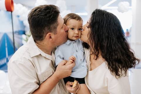Foto dos avós beijando o neto em momento de carinho.'
