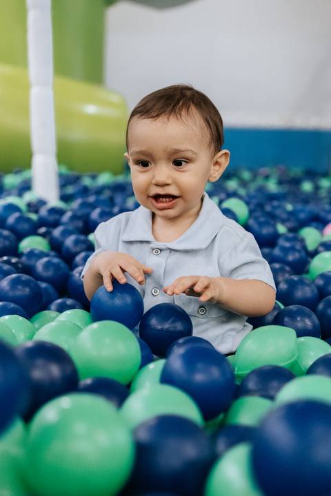 Foto do aniversariante brincando na piscina de bolinhas verde e azul.'