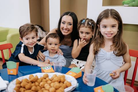 Foto aproximada de crianças e adultos reunidos na mesa da festa.'