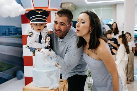 Foto do casal soprando a vela do bolo de 1 ano com o filho.'