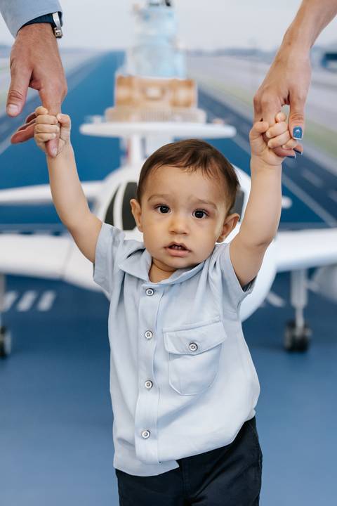 Foto do aniversariante erguendo os braços em frente à decoração da festa.'