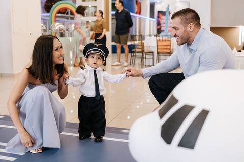 Foto dos pais brincando com o pequeno piloto entrando na festa.'