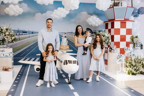 Foto da família reunida atrás do avião na mesa do bolo.'