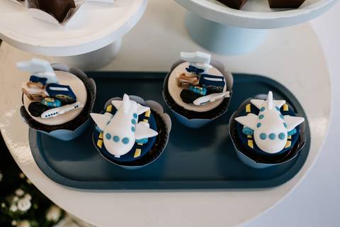 Foto aproximada de cupcakes decorados com pequenos aviões azuis.'