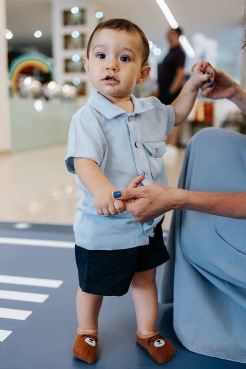 Foto em detalhe das mãos da mãe guiando o aniversariante.'