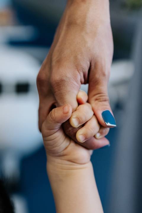 Foto em macro das mãos do aniversariante segurando o dedo da mãe.'