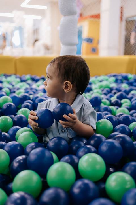 Foto do aniversariante brincando na piscina de bolinhas verde e azul.'