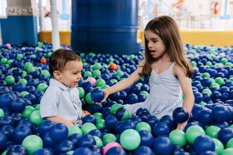 Foto do aniversariante brincando na piscina de bolinhas com a irmã.'