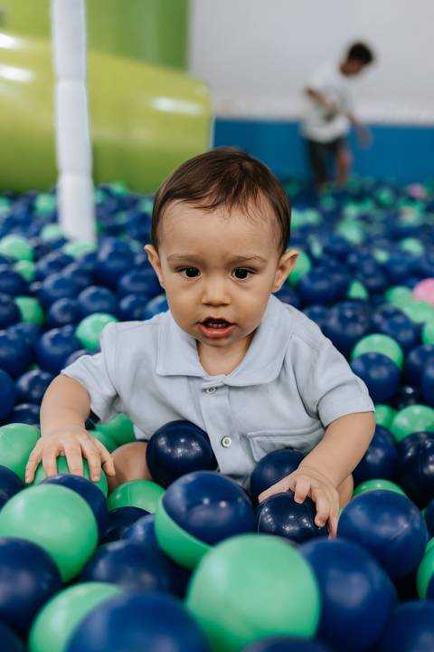 Foto de close do aniversariante rindo na piscina de bolinhas.'