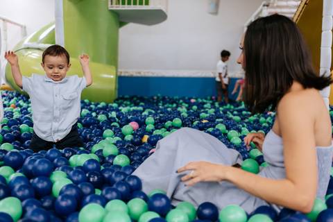 Foto da mãe agachada brincando com o filho na piscina de bolinhas.'